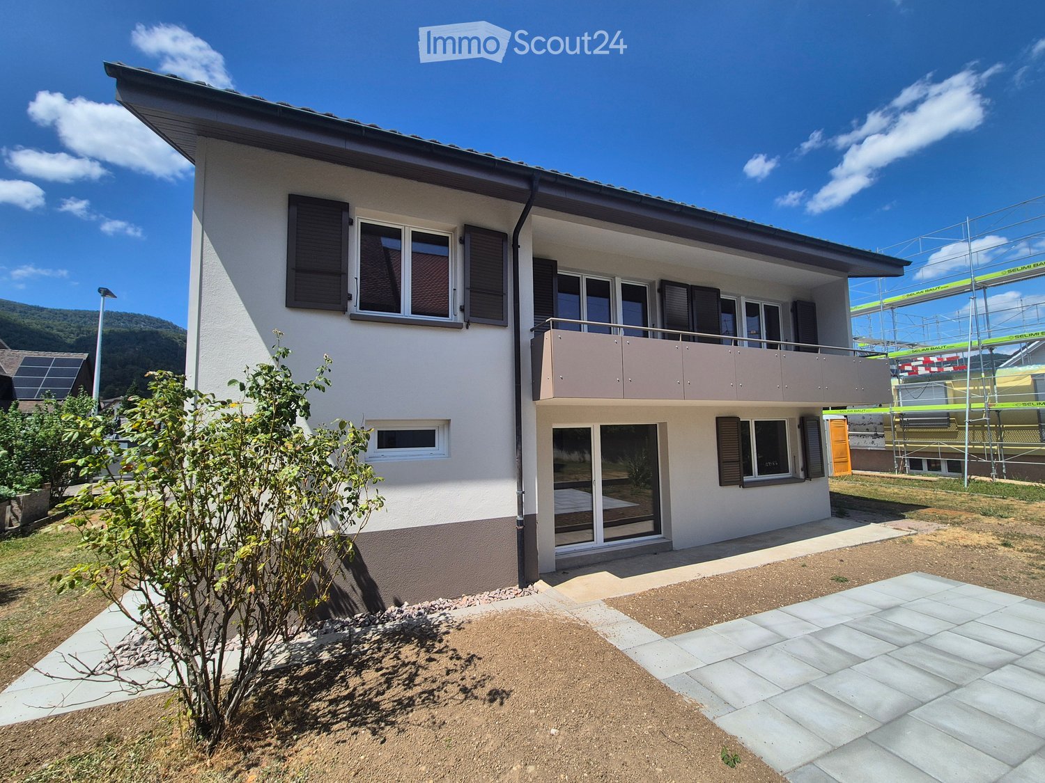 Two-story house with white exterior, multiple windows, balcony on the upper level, and solar panels on the roof.