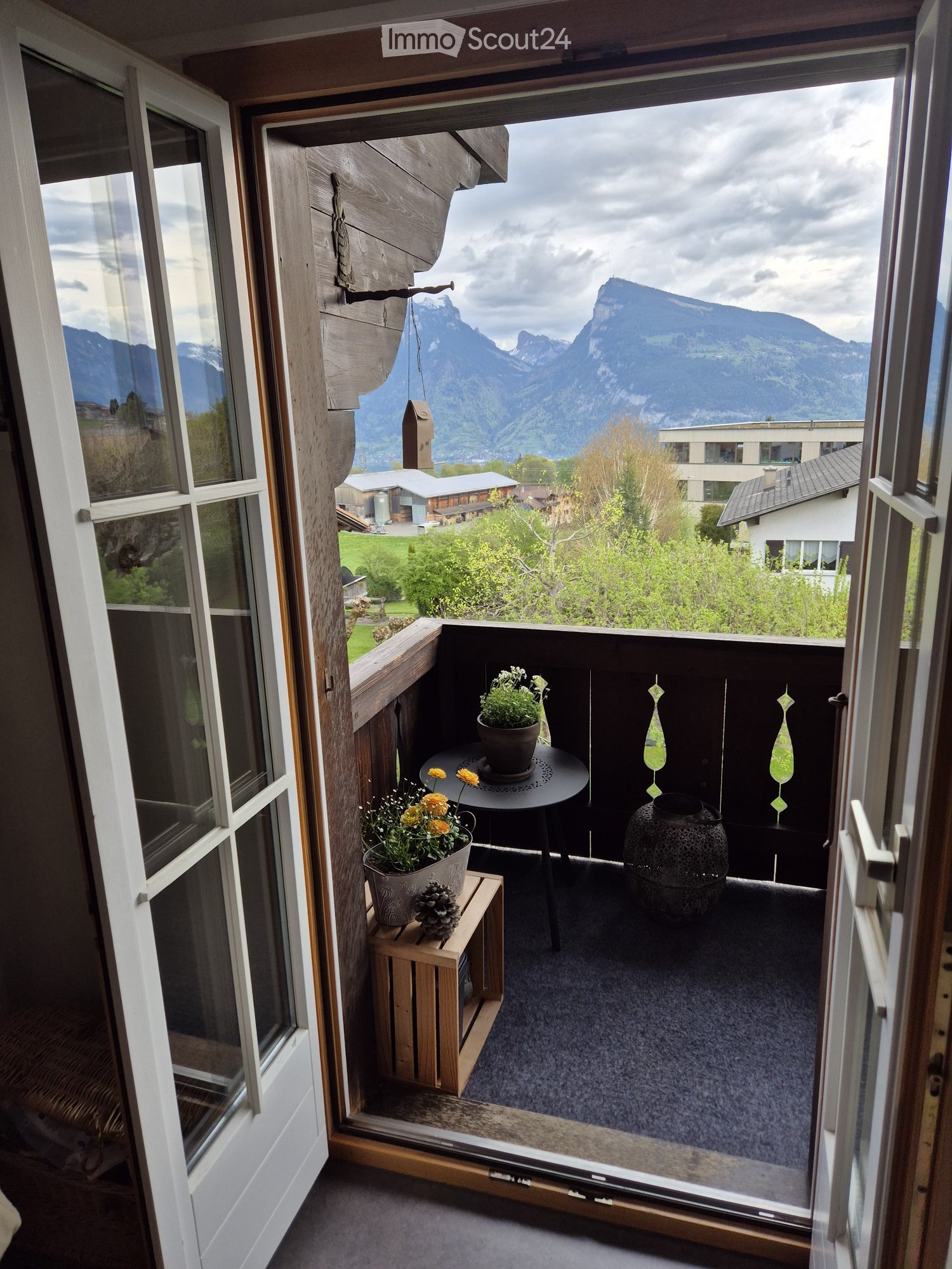 Balcony with a scenic mountain view, featuring a small round table, two flower pots, a wooden stool, and decorative vases.