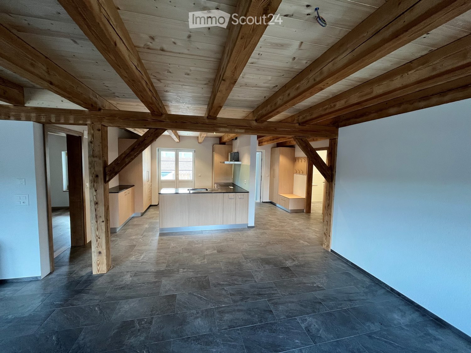 Open-plan kitchen with exposed wooden beams, dark tiled floor, light-colored cabinets, and a central island.