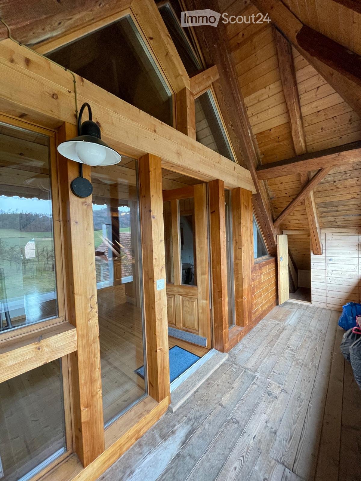 Wooden hallway with large windows, exposed wooden beams, and a modern wall-mounted light fixture.