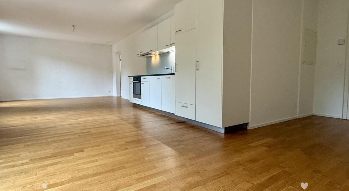 Empty room with light wooden flooring and white kitchen cabinets, no furniture or appliances present.