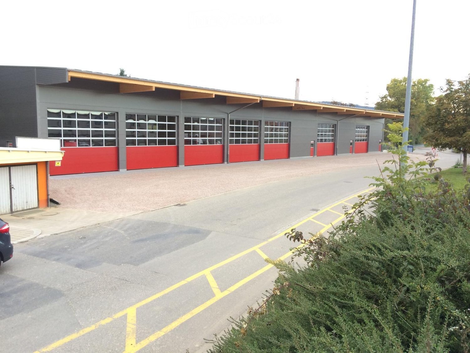 Modern building with multiple garage doors, grey exterior, yellow accents, and a paved parking area.