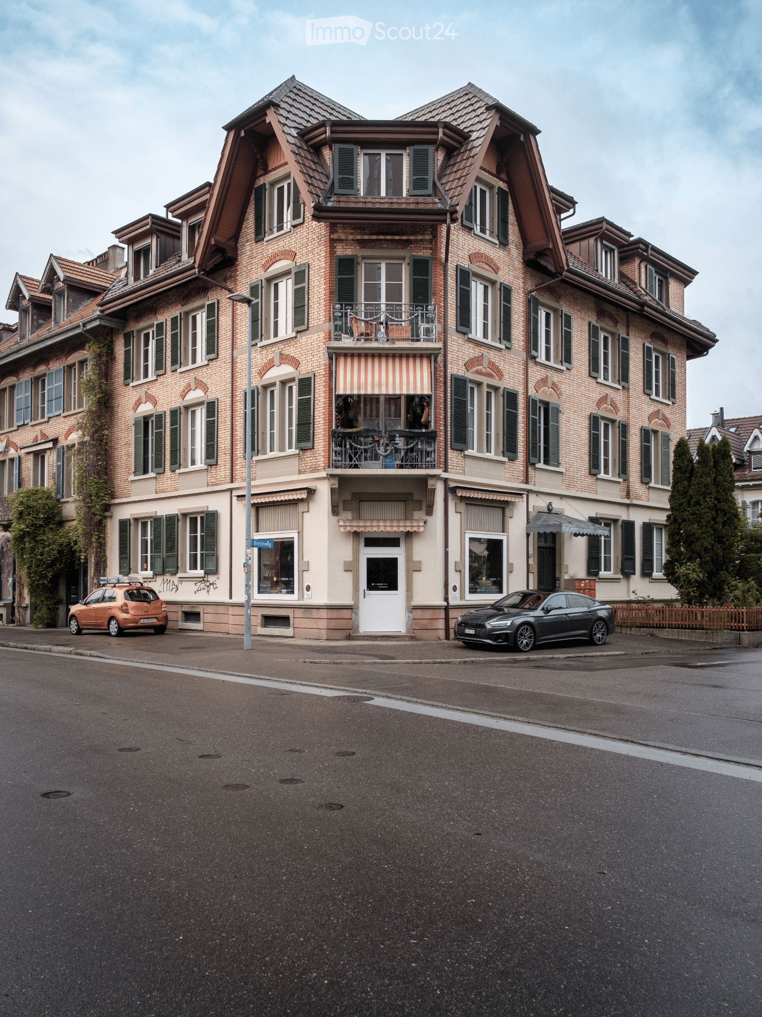 3 story brick building, large windows, awnings, balconies, cars parked in front