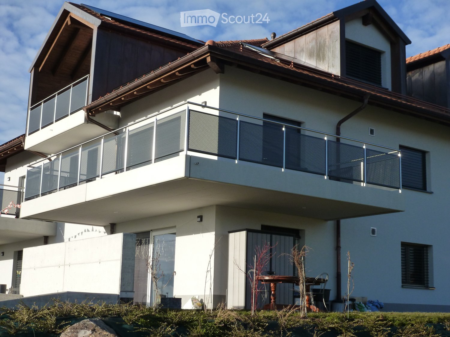 Two-story house with a balcony, modern design, and a small outdoor seating area with a table and chairs.