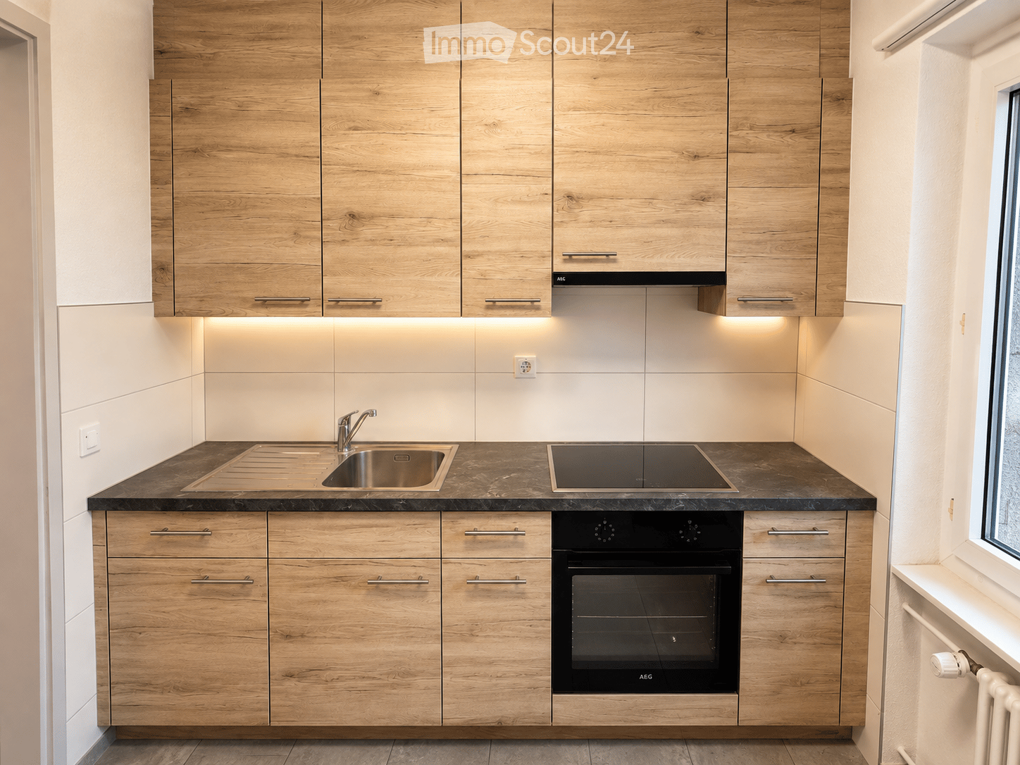 Modern kitchen with light wooden cabinets, stainless steel sink, electric stovetop, and built-in oven.