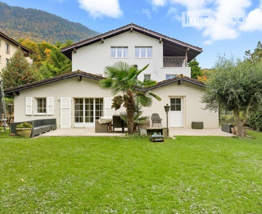 Two-story white house with a balcony, surrounded by a well-maintained lawn, palm tree, and outdoor seating area.