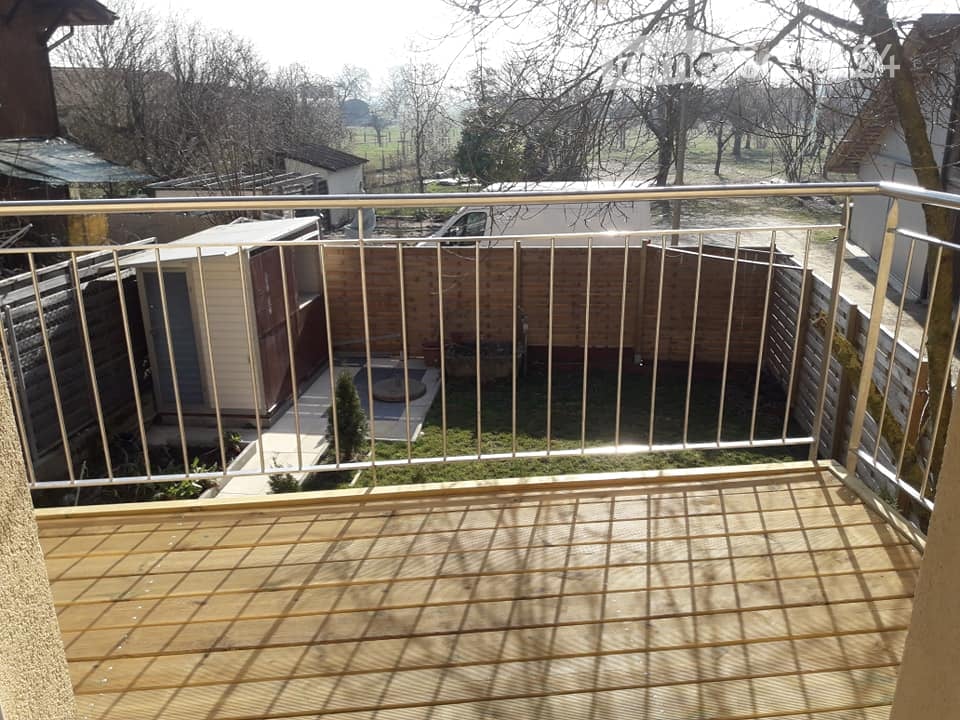 Balcony with wooden decking and metal railing, overlooking a fenced yard with a small pool and surrounding structures.