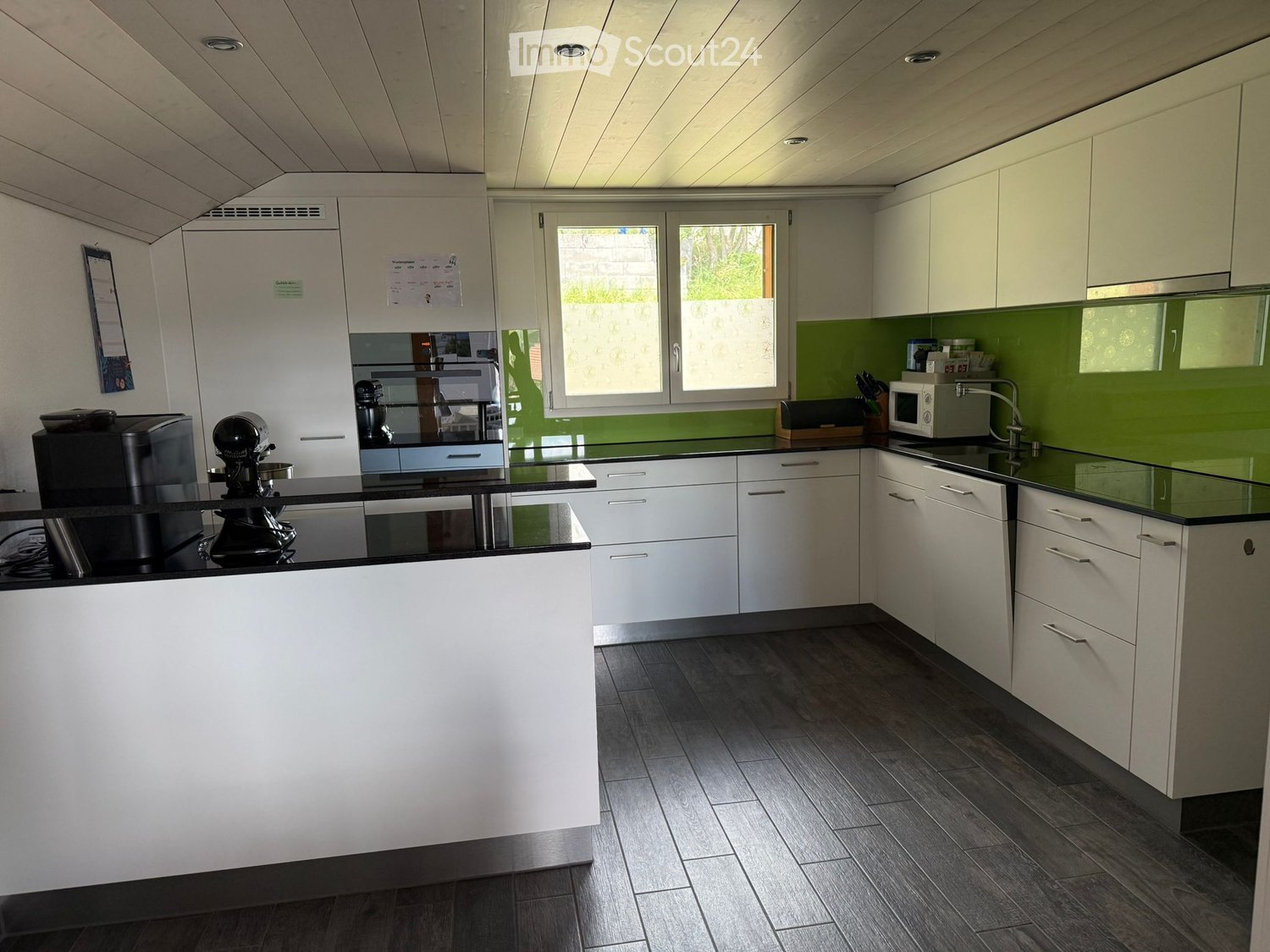 Modern kitchen with white cabinets, black countertops, and stainless steel appliances. Features a coffee maker, microwave, and a central island with a black countertop.
