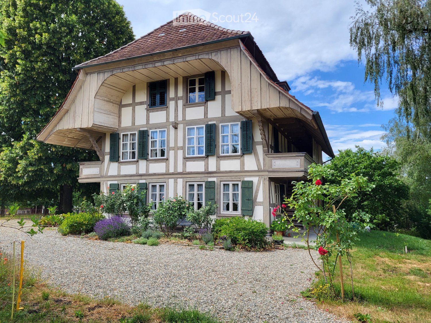 Two-story traditional house with wooden facade, green shutters, and a well-maintained garden.