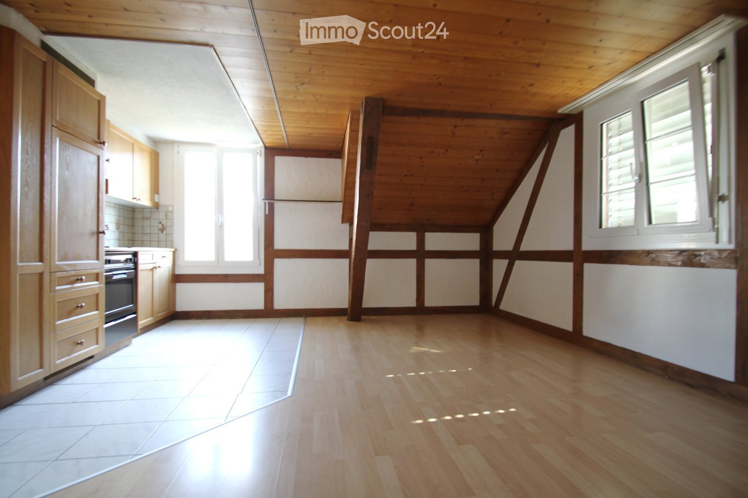 Empty room with wooden floor, white tiles, wooden beams, wooden cabinets, and windows.