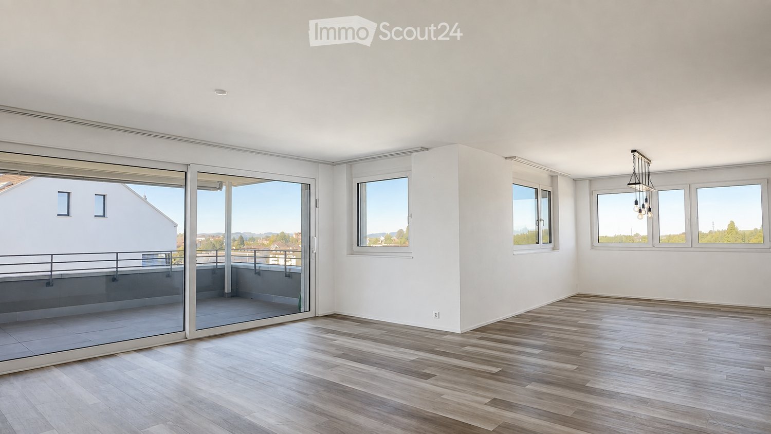 Empty room with wooden flooring, large windows, and a sliding glass door leading to a balcony.