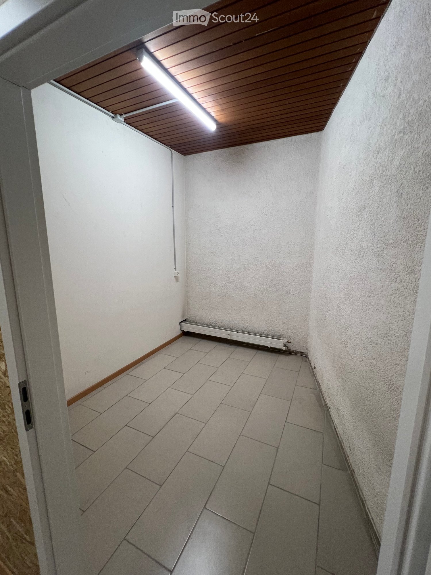 Empty hallway with tiled floor, white walls, wooden trim, and a wooden ceiling with integrated lighting. A radiator is mounted on one wall.