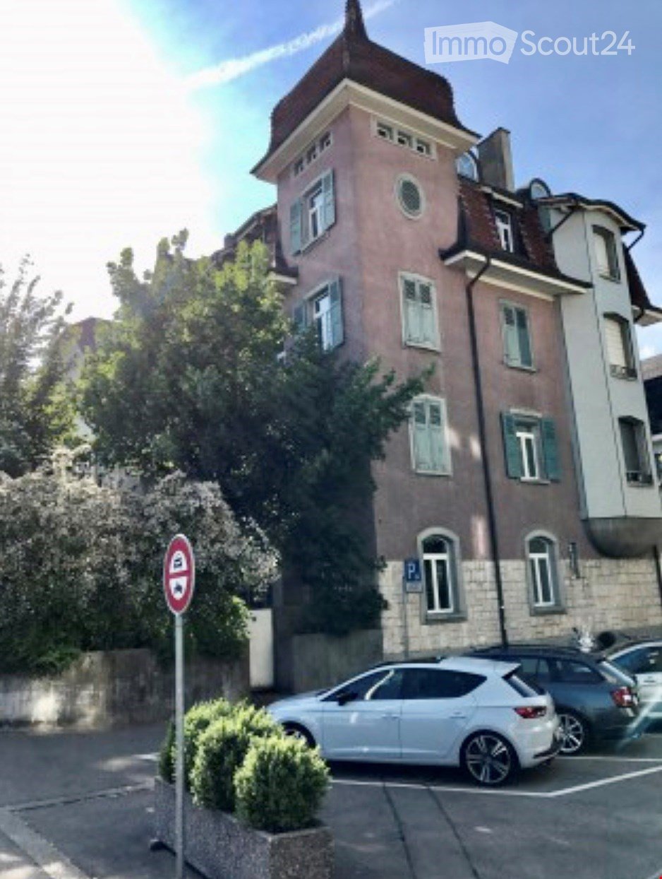 Multi-story residential building with pink facade, multiple windows, and a small garden area in front.
