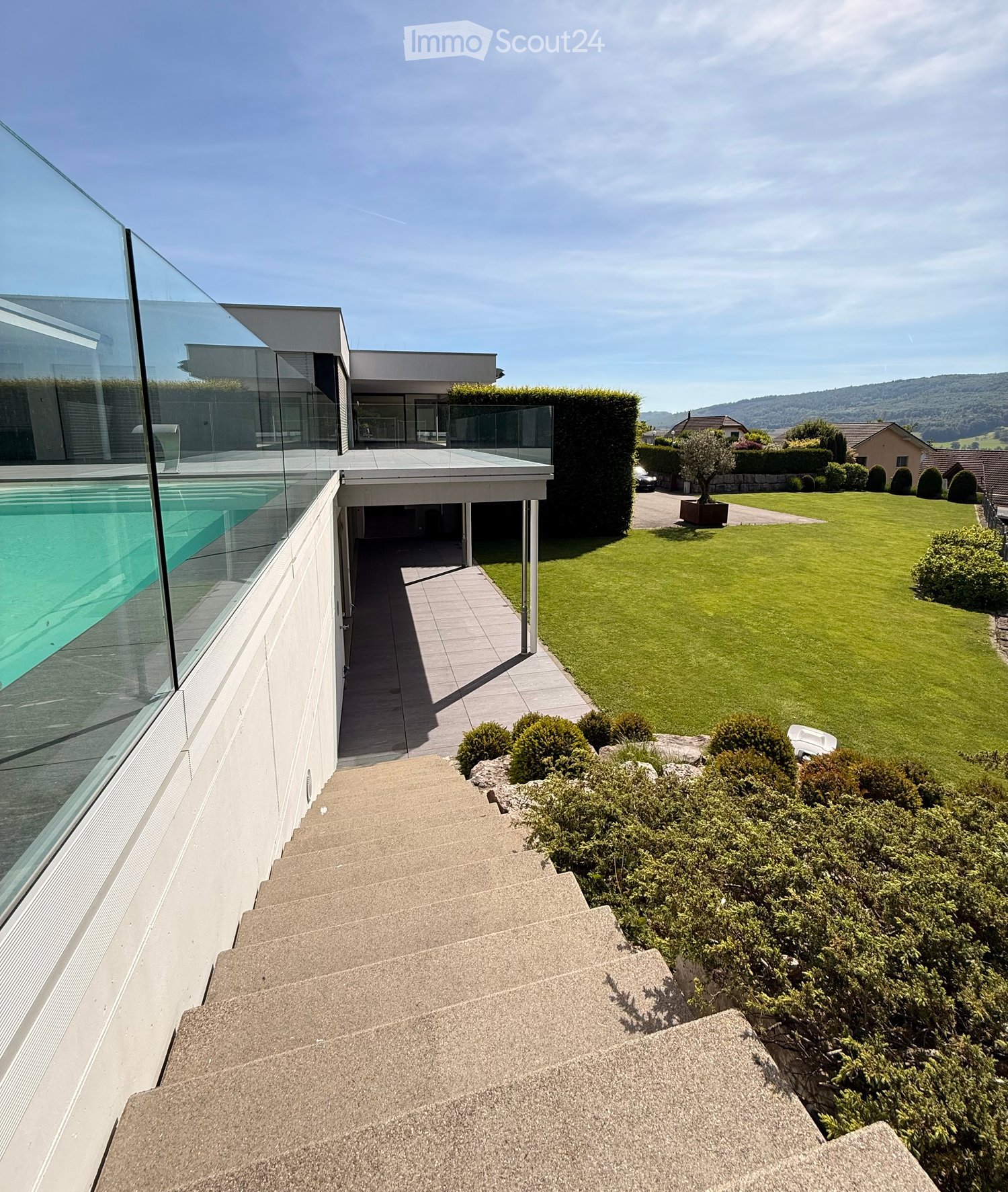 Modern house with a swimming pool, steps leading up to the house, well-maintained lawn, and surrounding greenery.
