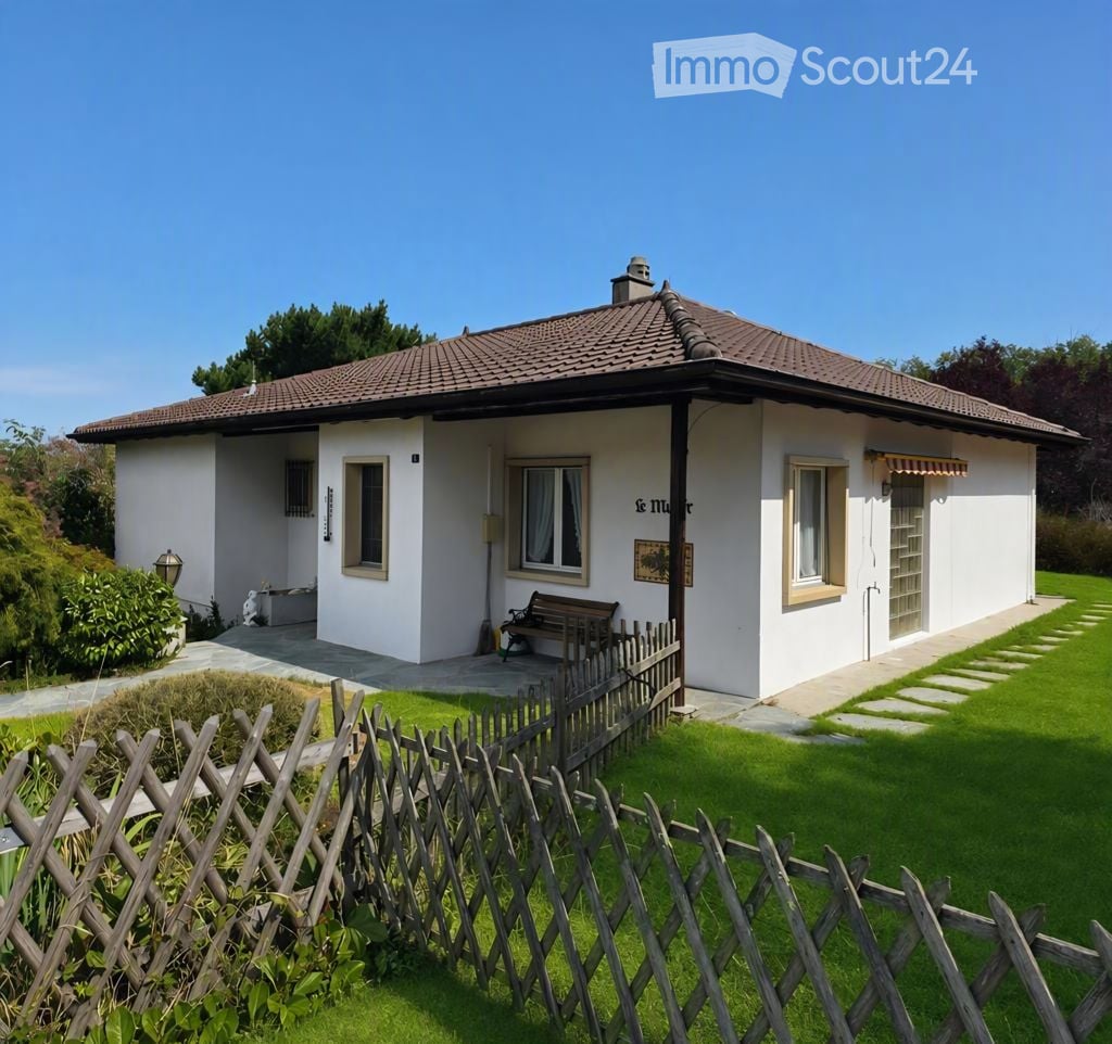 Single-story white house with a tiled roof, surrounded by a wooden fence and green lawn.