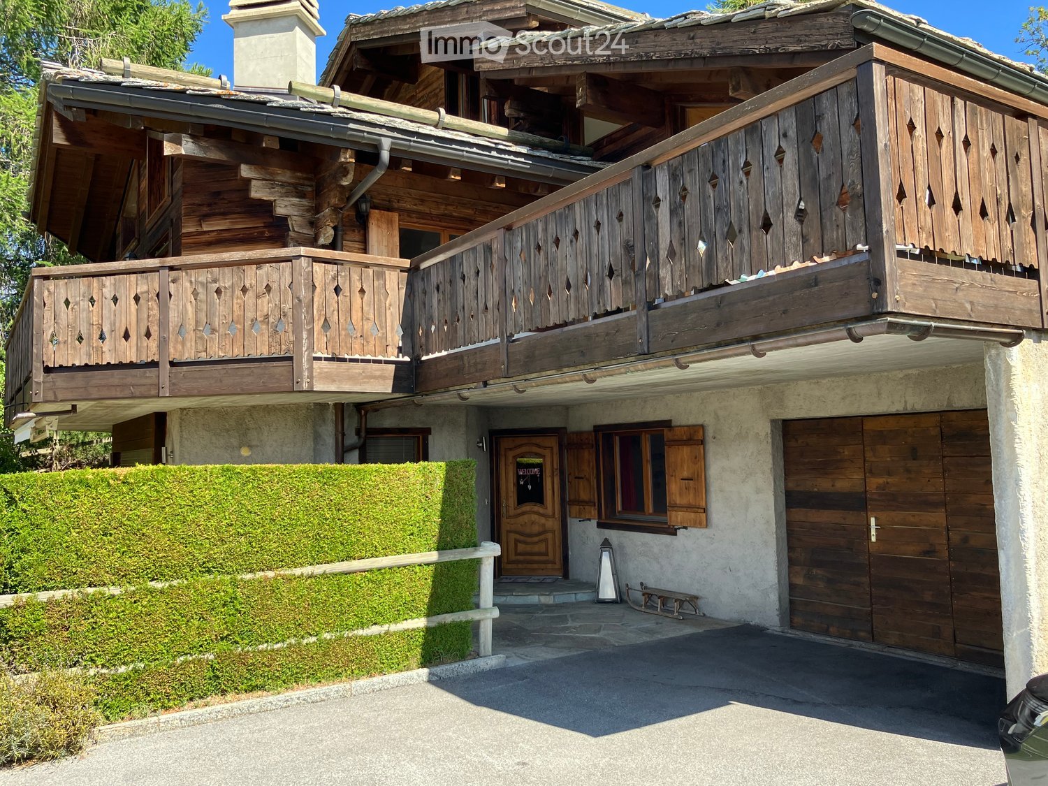 A two-story wooden house with a balcony, garage, and well-maintained garden.