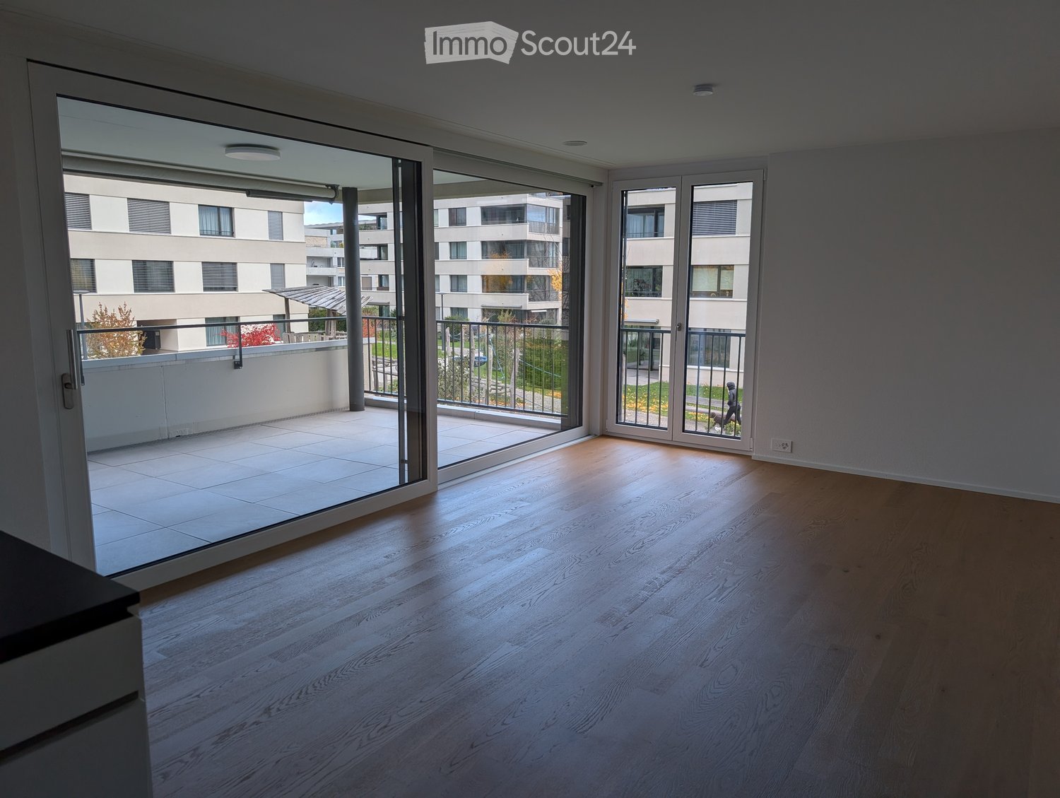 Empty room with wooden flooring and large glass sliding doors leading to a balcony. The balcony has a tiled floor and metal railing.