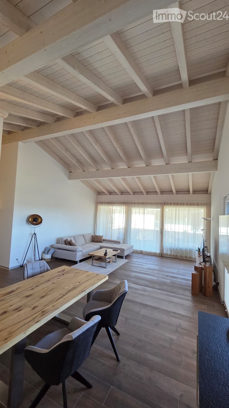 Open-concept living and dining area with exposed wooden beams, white sofa, coffee table, dining table, and chairs.