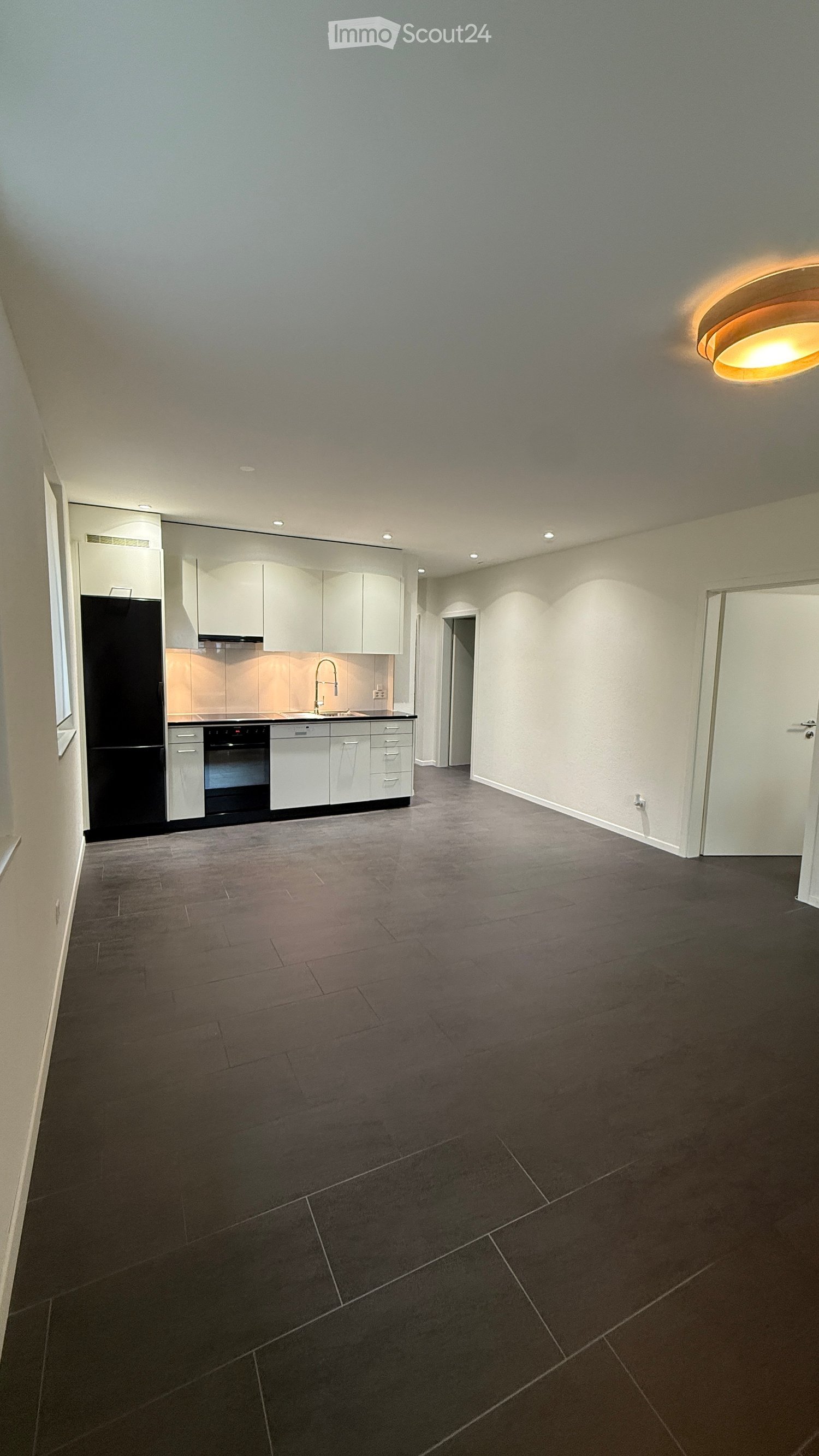 Empty kitchen with white cabinets, black appliances, and dark tiled flooring.