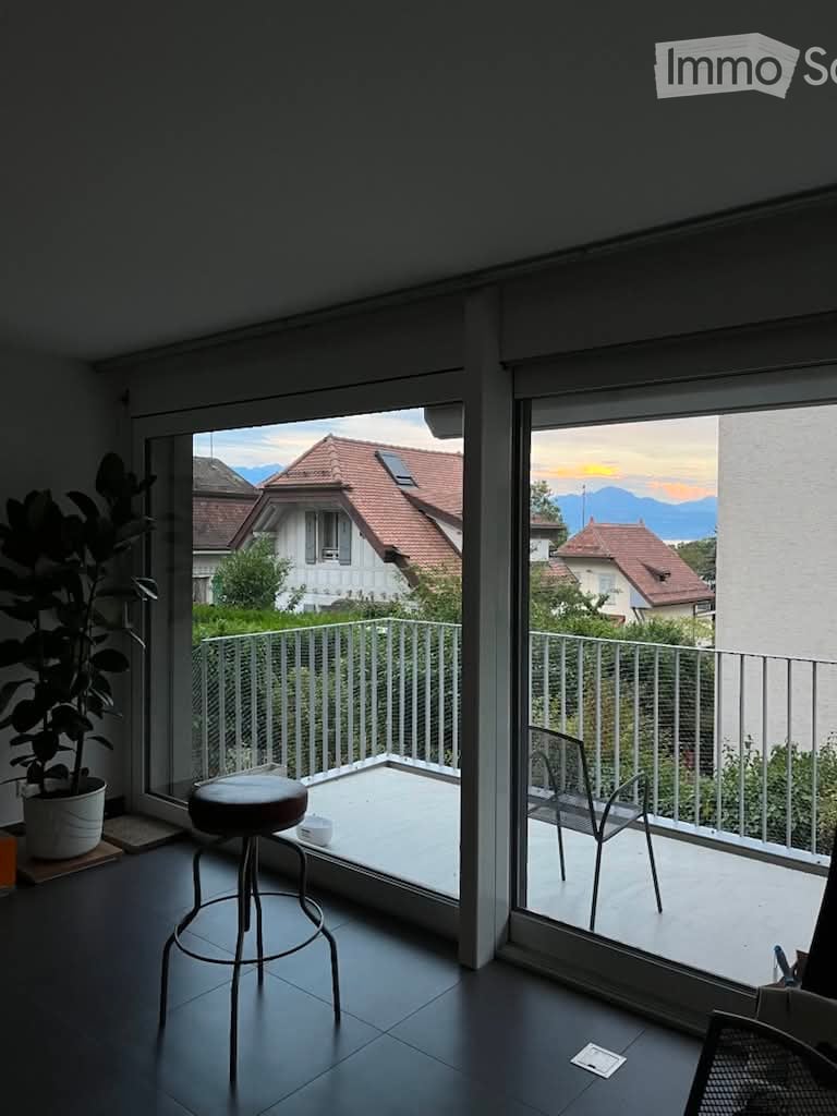 Modern room with large glass doors opening to a balcony, featuring a stool, chair, and potted plant, overlooking a scenic mountain view.