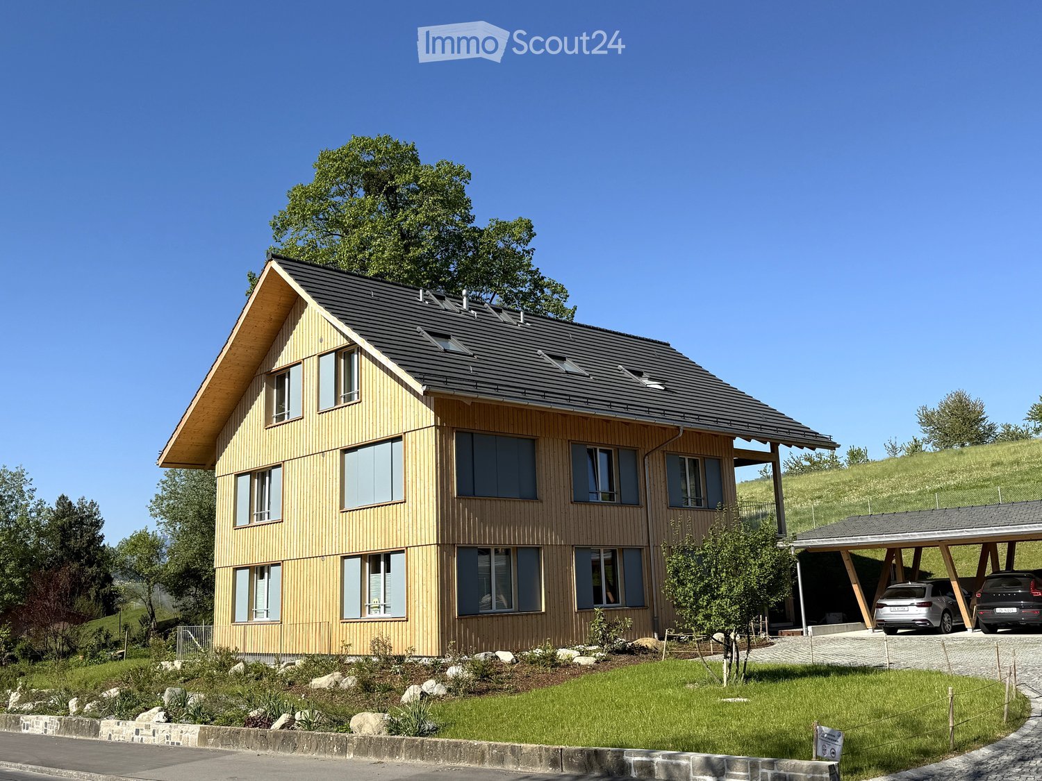 Modern two-story house with wooden siding, large windows, and a covered garage for two cars.