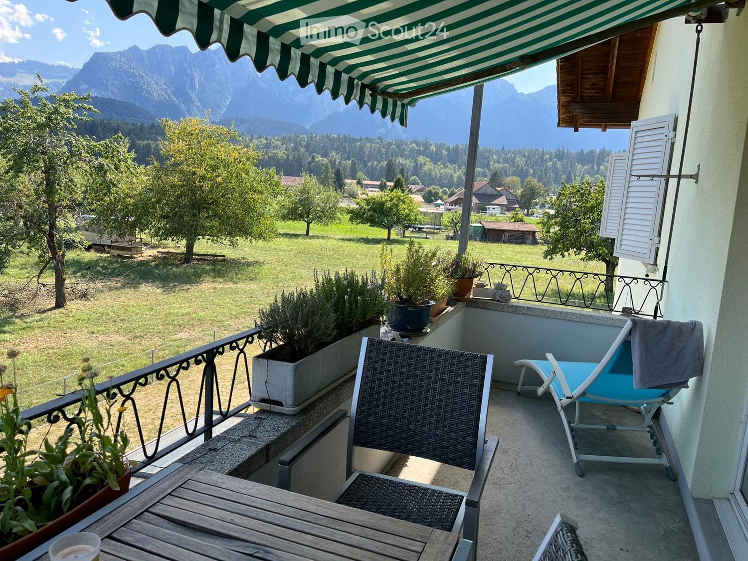 Balcony with a view of mountains, featuring a wooden table, two chairs, and potted plants.