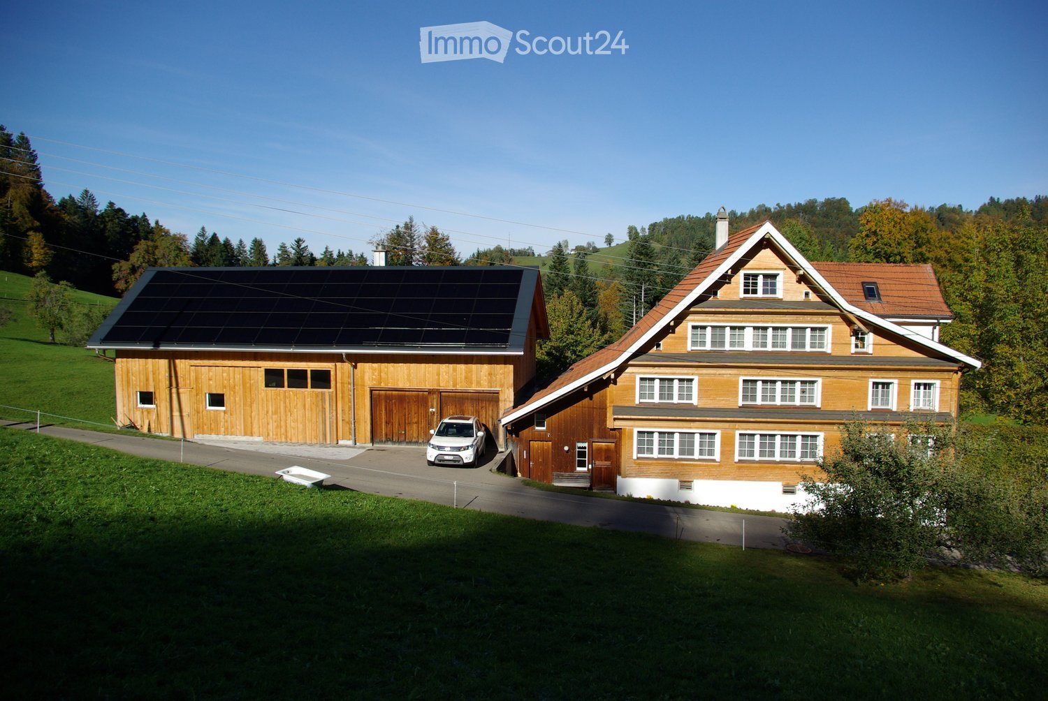 Two-story wooden house with a garage, solar panels on the roof, and a parking area.