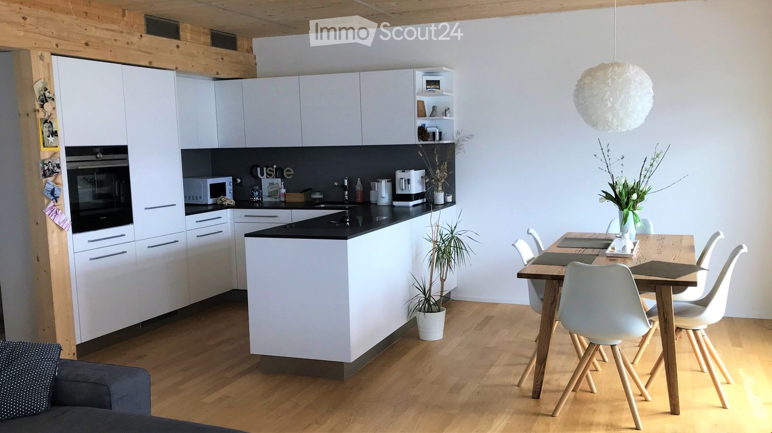 Modern kitchen and dining area with white cabinets, black countertops, a central island, a dining table with chairs, and a pendant light.