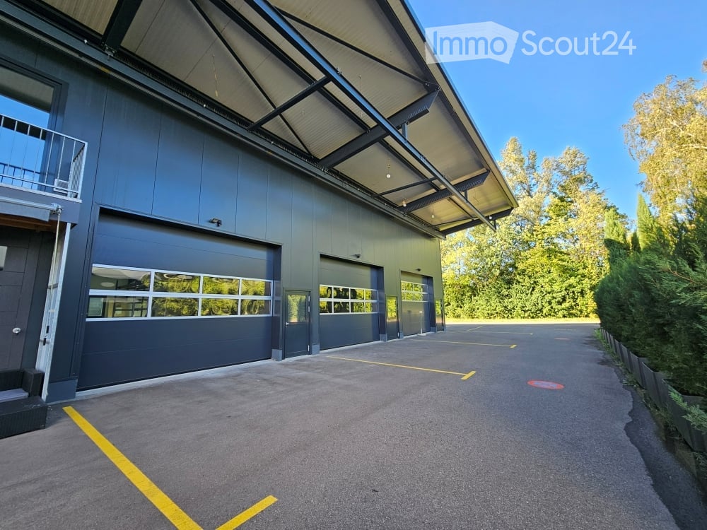 Modern industrial-style building with large garage doors, a covered walkway, and a spacious parking area.