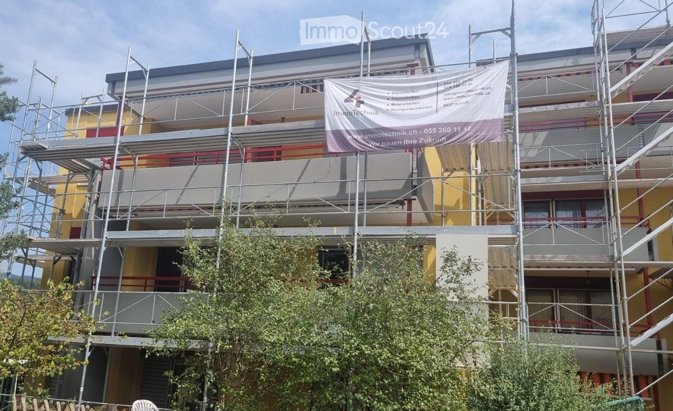 Multi-story building under construction with scaffolding, yellow facade, and a banner advertising renovation services.