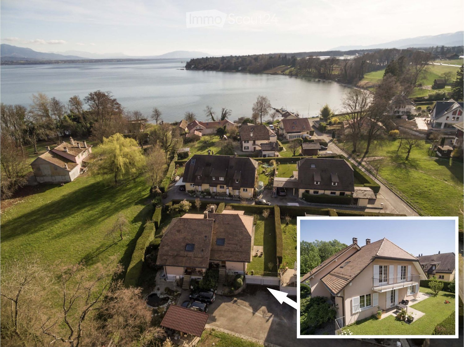 Aerial view of a residential area with multiple houses, surrounded by green lawns, trees, and a lake in the background.