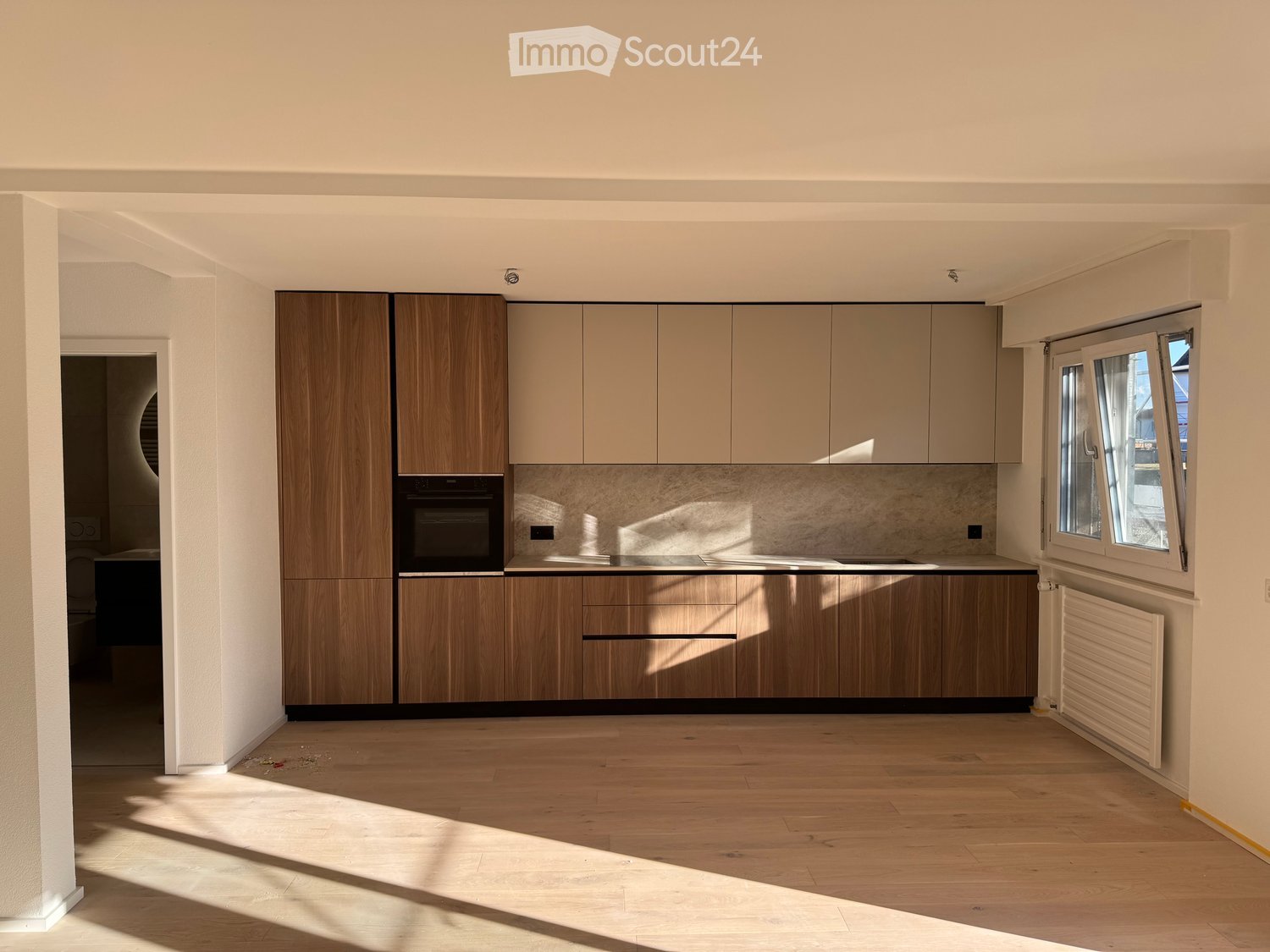 Modern kitchen with light wood cabinets, stainless steel oven, and wooden flooring.