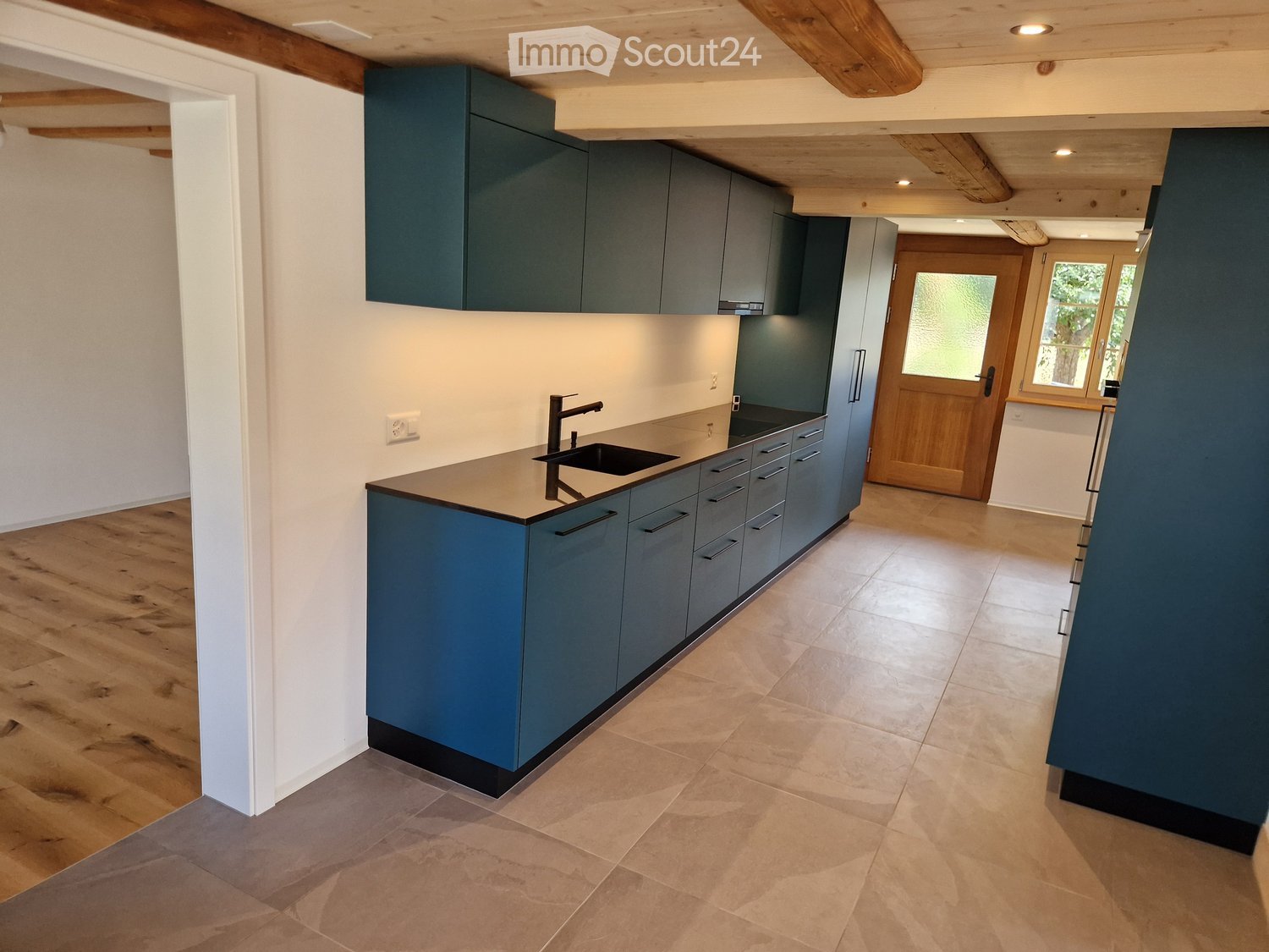 Modern kitchen with blue cabinets, a central island, and a sink. The space features wooden flooring and a wooden door leading outside.