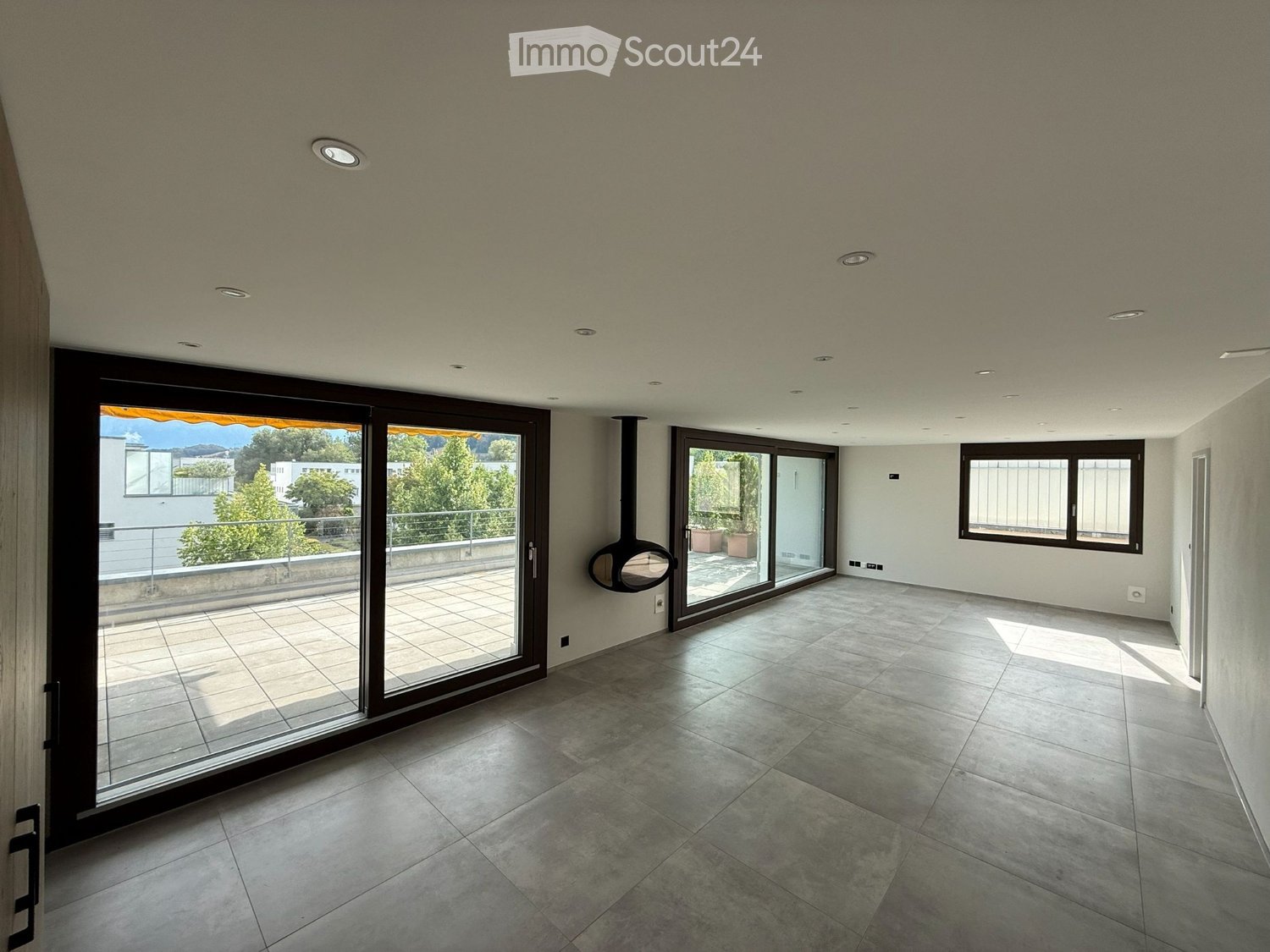 Empty room with tiled floor, large sliding glass doors leading to a balcony, and recessed ceiling lights.