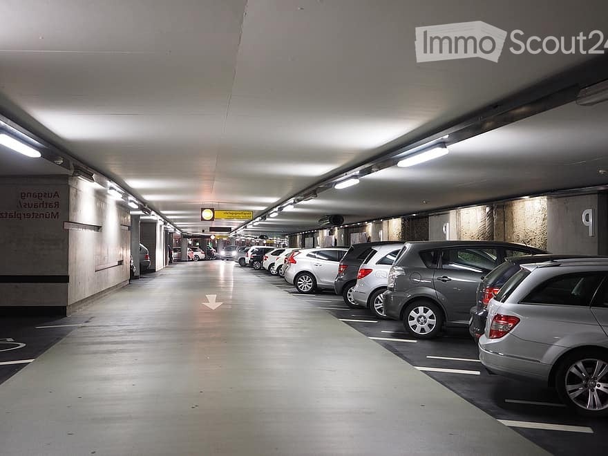 Underground parking area with multiple parked cars, fluorescent lighting, and directional signage.