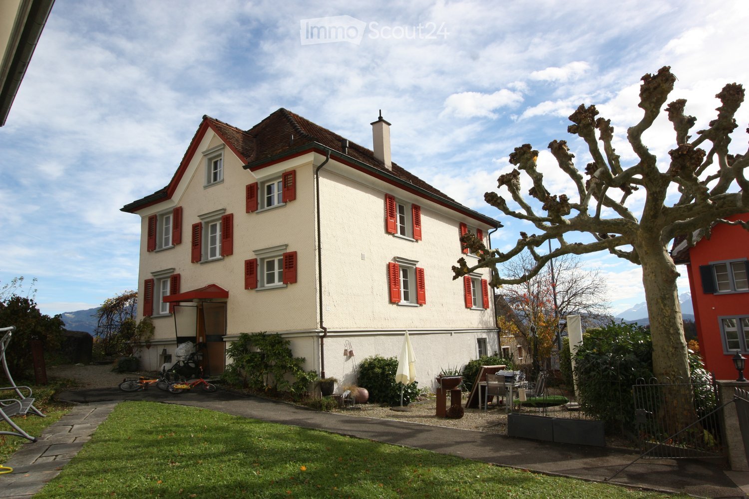 Traditional house with multiple windows, chimney, well-maintained garden, lawn, trees, and a view of the mountains.