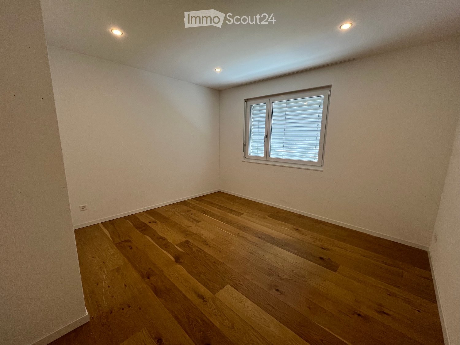 Empty room with light wooden flooring, white walls, and a single window with blinds.