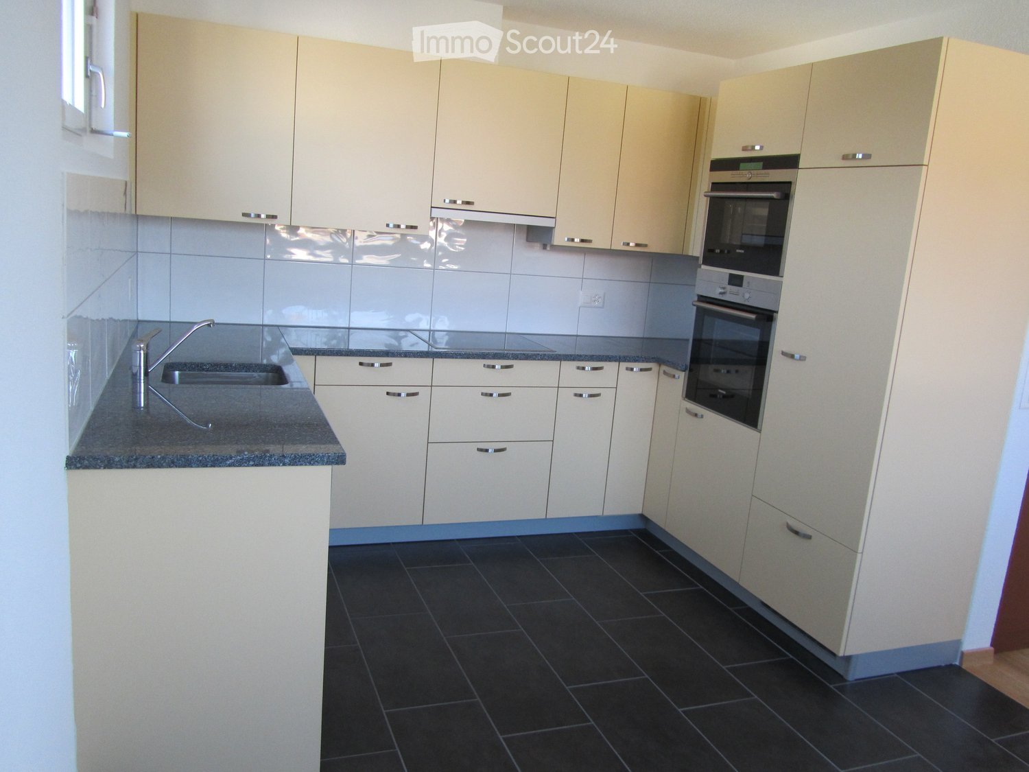 Modern kitchen with light-colored cabinets, dark tiled floor, granite countertop, and built-in oven.