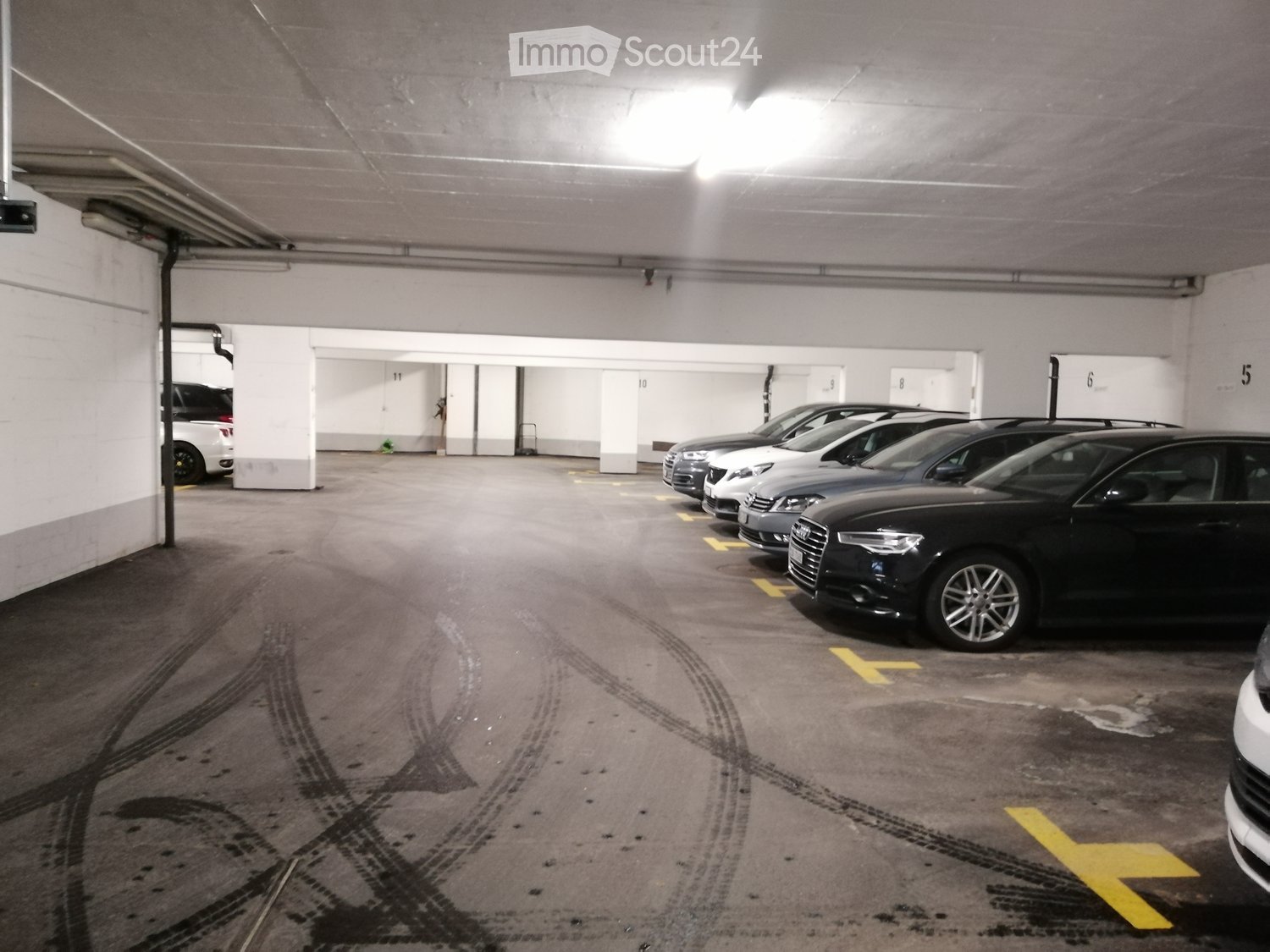Empty parking garage with white walls, cars parked, ceiling lights, yellow parking lines