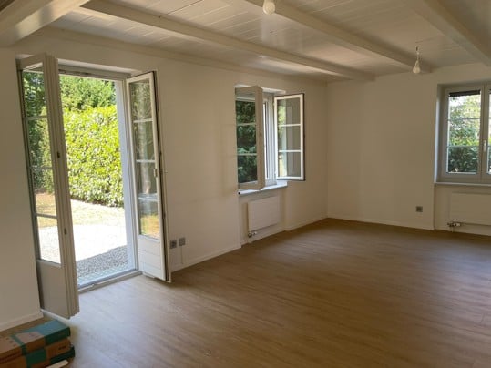 Empty room with wooden flooring, white walls, large windows, and a sliding glass door leading to an outdoor area.