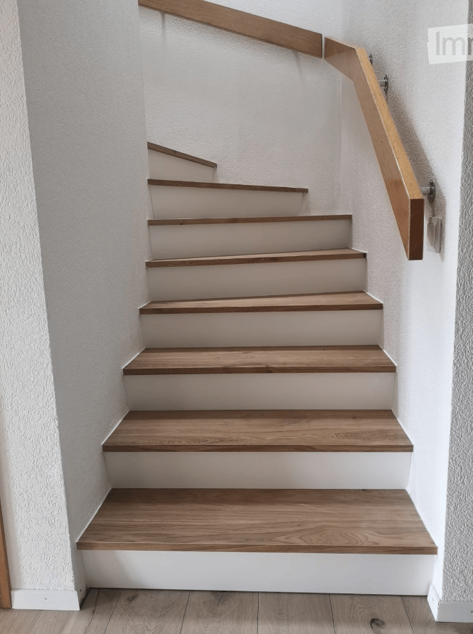 A modern staircase with wooden steps and a matching wooden handrail, set against white walls.