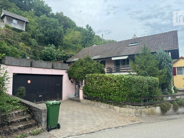 Two-story house with a garage, surrounded by greenery and a small garden area.