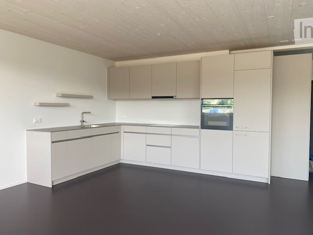 Modern, minimalist kitchen with white cabinets, a central island, and a built-in oven. The space features sleek, contemporary design elements and ample storage.