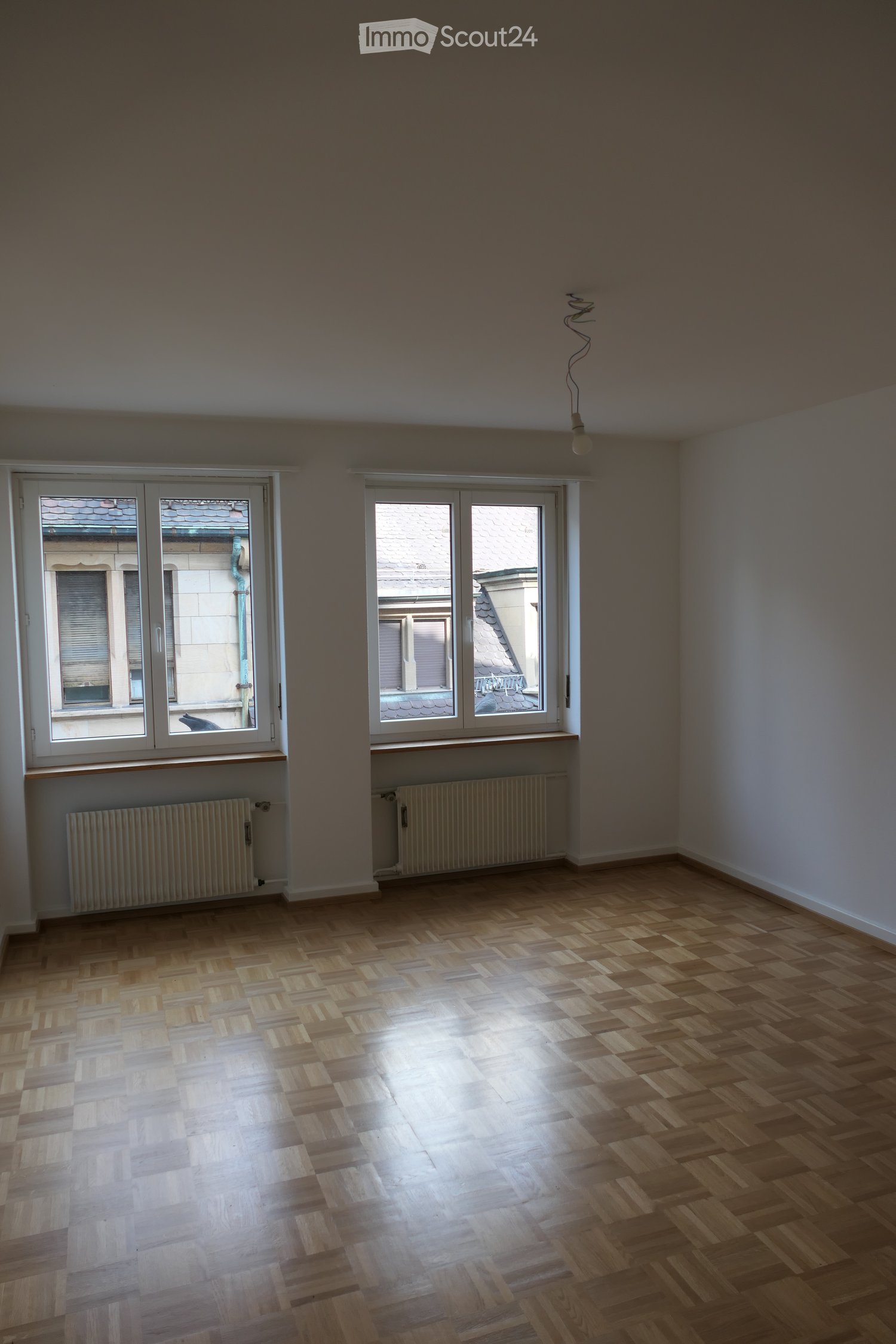 empty room, wooden parquet floor, white walls, two large windows, white radiators