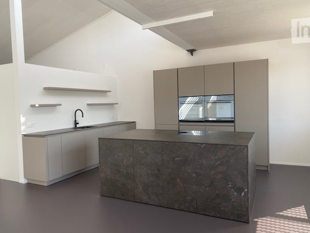 Modern kitchen with sleek, minimalist design featuring a large central island with a dark marble countertop, integrated sink, and modern cabinetry.