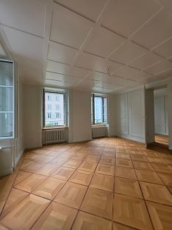 Completely empty room with wooden flooring, white walls, and large windows. No furniture or equipment.