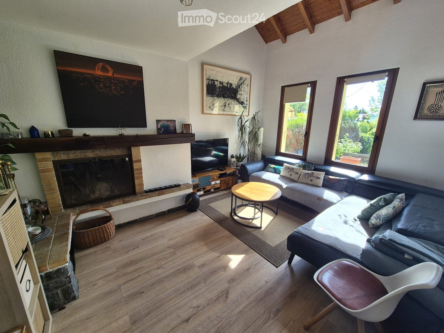 Modern living room with wooden flooring, large windows, fireplace, sofa, coffee table, and decorative items.