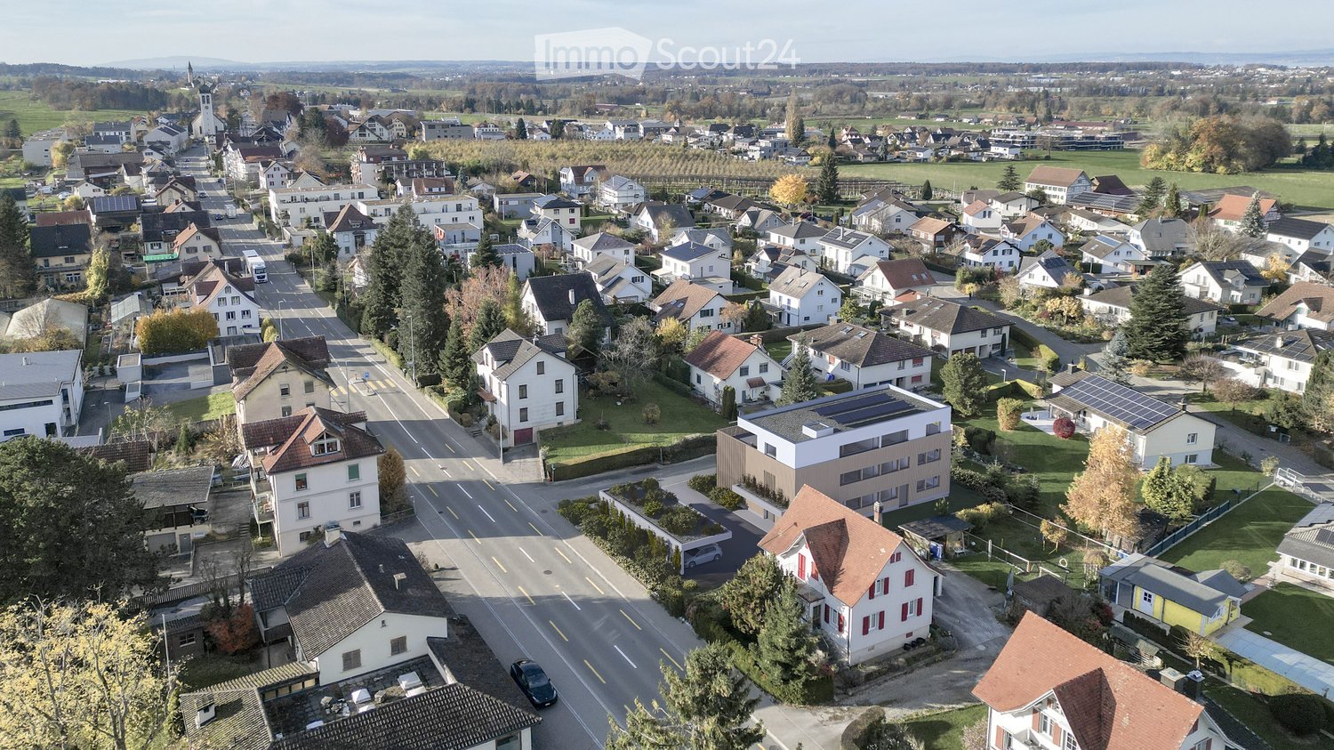 Aerial view of a suburban neighborhood with multiple houses, roads, trees, and a distant landscape.