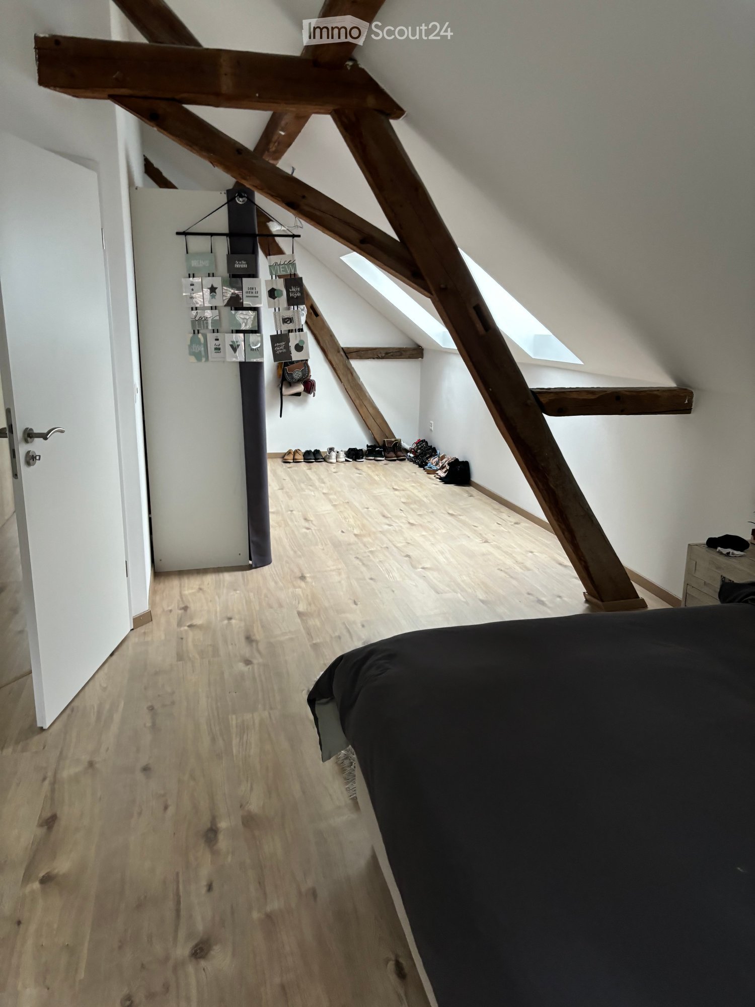 Bright attic bedroom with wooden beams, skylights, wooden flooring, and a bed partially visible.