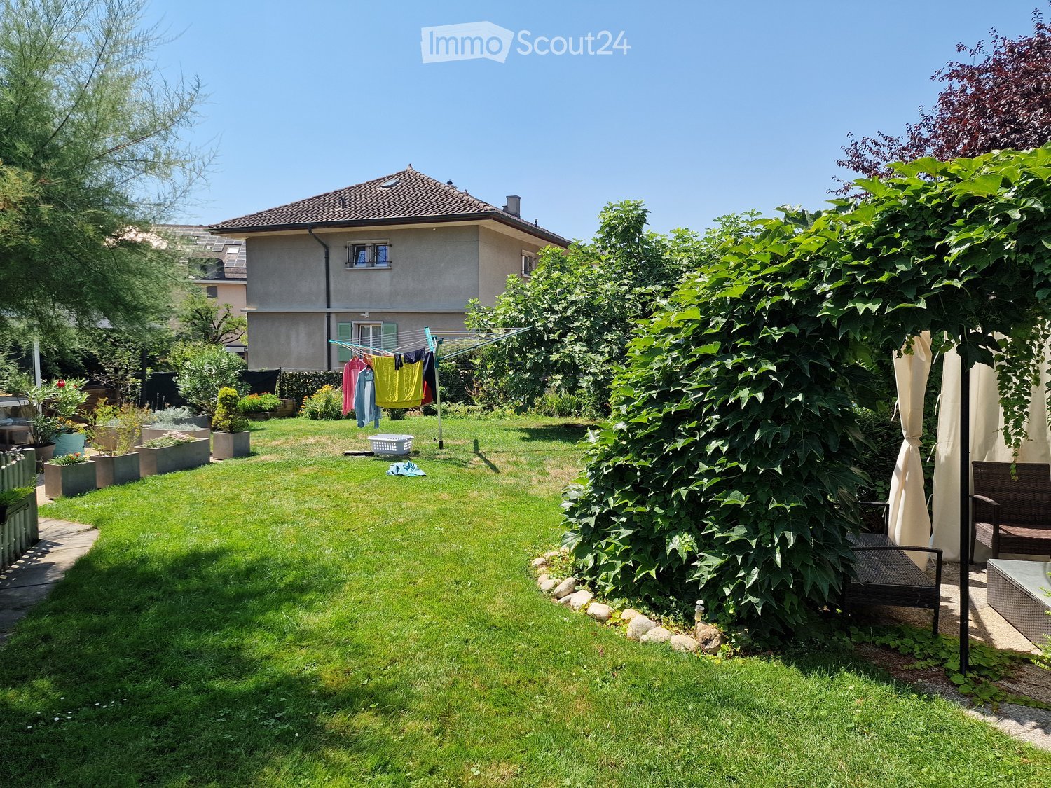 Well-maintained garden with a lawn, potted plants, a clothesline with laundry, and a small seating area with outdoor furniture.
